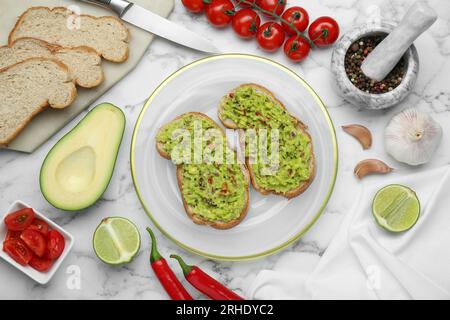 Deliziosi panini con guacamole e ingredienti su un tavolo in marmo bianco, piatti Foto Stock