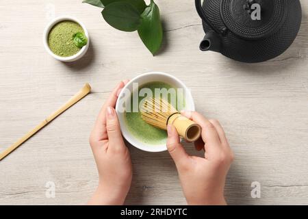 Donna che prepara tè matcha con frusta di bambù al tavolo di legno, vista dall'alto Foto Stock