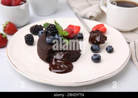 Piatto con delizioso fondente di cioccolato, frutti di bosco e menta su tavolo bianco, primo piano Foto Stock