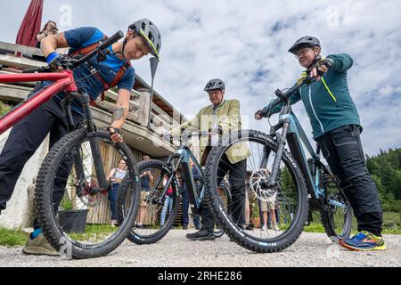 16 agosto 2023, Baviera, Aschau IM Chiemgau: Joachim Herrmann (M), (CSU) Ministro di Stato per l'interno, lo sport e l'integrazione, siede su una bicicletta elettrica durante un appuntamento per i media sul Kampenwand. A sinistra, un poliziotto gli mostra ciò che i ciclisti devono fare in montagna; a destra Klaus Stöttner, MDL e primo presidente del Consiglio bavarese di Trustees for Alpine Safety e. V. Herrmann si è informato sul Kampenwand sugli argomenti: statistiche sugli incidenti alpini, "mountain bike sicura" e "equipaggiamento di sicurezza per via ferrata". C'è stata anche una dimostrazione Foto Stock