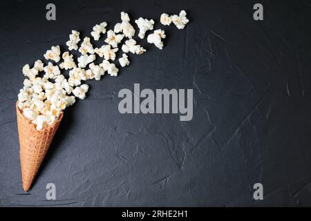 Cono waffle con popcorn salato su fondo nero di cemento. Primo piano sullo spuntino Foto Stock