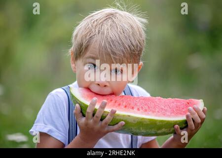 Fantastico bambino biondo, ragazzo con cane, anguria in giardino, estate Foto Stock