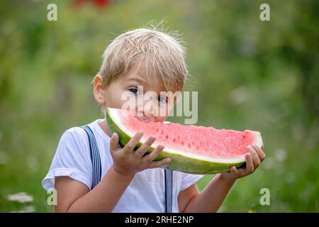 Fantastico bambino biondo, ragazzo con cane, anguria in giardino, estate Foto Stock
