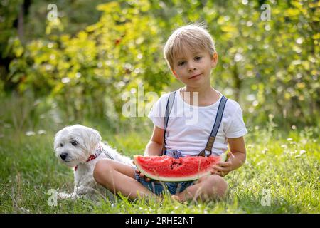 Fantastico bambino biondo, ragazzo con cane, anguria in giardino, estate Foto Stock