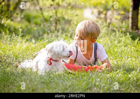 Fantastico bambino biondo, ragazzo con cane, anguria in giardino, estate Foto Stock