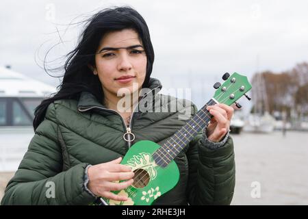 giovane donna venezuelana, felice giocando imparando a giocare a ukulele, in piedi guardando la macchina fotografica, in argentina viaggi all'aperto, concetto di stile di vita, copia spac Foto Stock