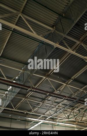 Parte del soffitto di un ampio magazzino o magazzino di un moderno impianto industriale o di una fabbrica rappresentata da strutture metalliche di colore grigio Foto Stock