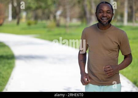 Uomo afroamericano maturo che fa jogging nel parco e sembra soddisfatto Foto Stock