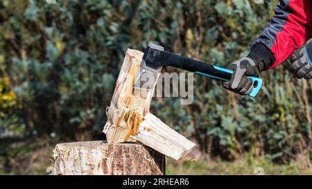 Ravvicinare un'ascia affilata nella mano umana quando si spaccano tronchi di legno sul blocco di trinciatura. Uomo di lavoro che tiene un moderno utensile da taglio con lama in metallo e innesto in plastica. Foto Stock