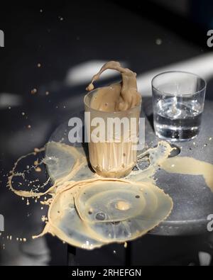 latte in tazza di vetro che cadde e versò il latte sul tavolo l'acqua congelata sullo sfondo grigio aria, su caffè da tavolo in cemento lucidato a moti Foto Stock