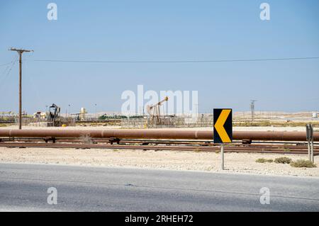 Infrastrutture per giacimenti petroliferi del Bahrein - tubi del petrolio, martinetto per pompe, cavallo per petrolio, martinetto per petrolio, pompa per travi che estrae petrolio greggio dai pozzi petroliferi. Segnaletica stradale Foto Stock