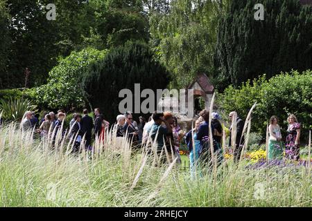 Una festa di nozze si riunisce a Southover Grange Gardens dopo aver visitato per la prima volta l'ufficio del registro come visto dietro gli alberi di tasso. Foto Stock