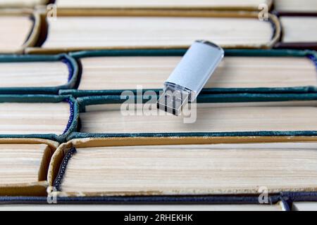 Scheda flash USB sullo sfondo di una grande pila di vecchi libri squallidi. Portabilità dei moderni supporti di archiviazione delle informazioni Foto Stock