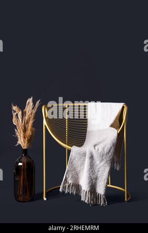 Elegante poltrona con coperta e pampas in vaso su sfondo nero Foto Stock