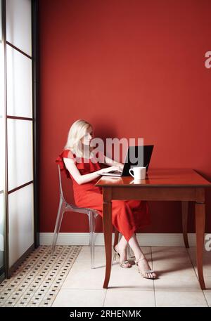 Bella giovane donna adulta che indossa un tuta rossa e un computer portatile funzionante Foto Stock