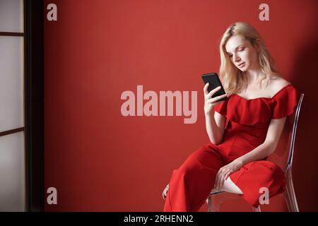 Giovane donna adulta che si rilassa su una sedia e usa lo smartphone Foto Stock