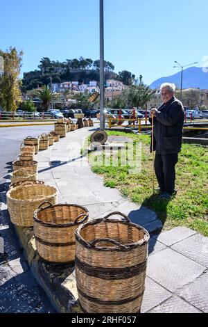 Uomo che vende cestini in vimini tessuti tradizionali per strada al mercato nel vecchio quartiere di Kalamata, Messinina, Poloponnese, Grecia. Foto Stock