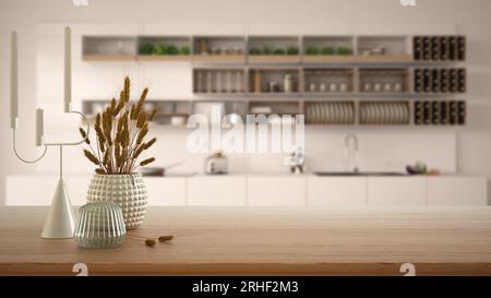 Tavolo, scrivania o scaffale in legno primo piano con vasi in ceramica e vetro con piante secche, cannucce su vista sfocata della cucina bianca con armadi e ripiani Foto Stock