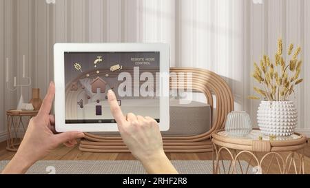 Sistema di controllo della casa con telecomando intelligente su un tablet digitale. Dispositivo con icone app. Soggiorno con carta da parati a righe, divano in rattan sullo sfondo, arco Foto Stock