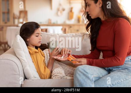 Mamma premurosa che dà pillola di farmaci alla figlia malata al coperto Foto Stock