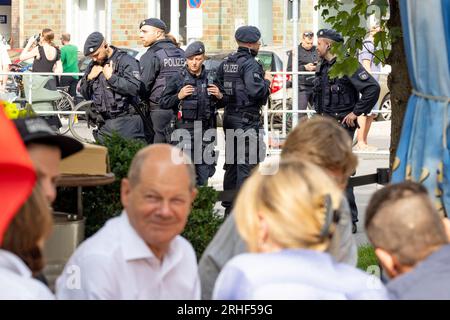 Duesseldorf, Germania. 16 agosto 2023. Il Cancelliere tedesco Olaf Scholz (L, fronte, SPD) parla con i cittadini di Düsseldorf davanti a un Büdchen, sullo sfondo gli ufficiali di polizia di una task force che assicura la visita del Cancelliere. Il Düsseldorf Büdchentag ha emesso l'invito. Credito: Christoph Reichwein/dpa/Alamy Live News Foto Stock