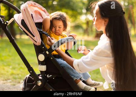 Mamma che si prende cura del comfort della figlia durante la passeggiata all'esterno di Stroller Foto Stock