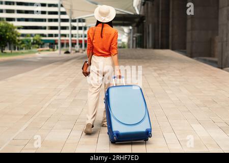 Vista posteriore della Tourist Lady Walking con valigia vicino all'aeroporto Foto Stock