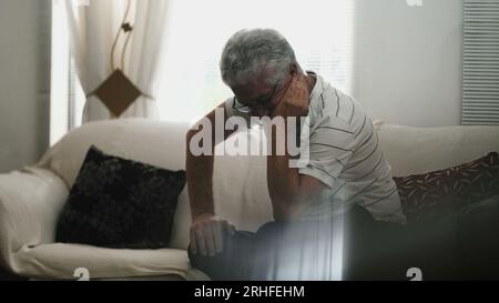 L'anziano sperimenta frustrazione e preoccupazione, da solo a casa nella scena di Candid, seduto sul divano in una tranquilla contemplazione Foto Stock