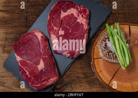 Due bistecche di ribeye con sale e pepe sullo sfondo nero del tagliere Foto Stock