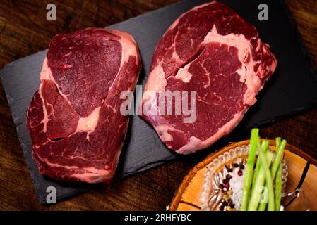 Due bistecche di ribeye con sale e pepe sullo sfondo nero del tagliere Foto Stock