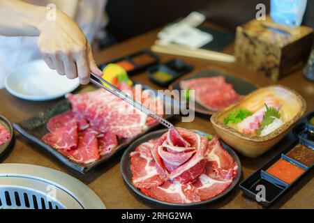 Woman's Hand utilizza pinze per posizionare il wagyu beef su un piatto, pronto per grigliare su carbone, migliorando l'esperienza culinaria in un ristorante giapponese Foto Stock