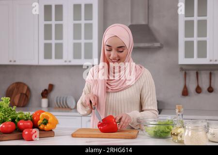 Donna musulmana che prepara una deliziosa insalata con verdure al tavolo bianco in cucina Foto Stock