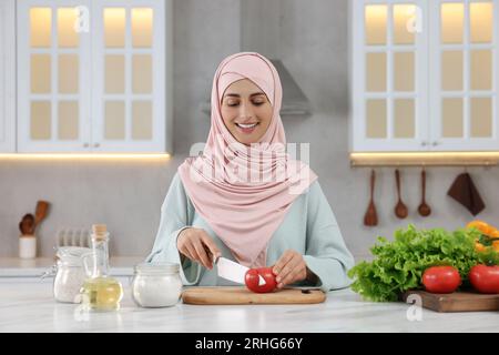 Donna musulmana che prepara una deliziosa insalata con verdure al tavolo bianco in cucina Foto Stock