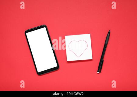 Concetto di relazione a distanza. Smartphone, note d'amore e penna su sfondo rosso, posizionamento piatto Foto Stock
