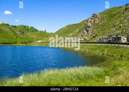 L'autostrada alpina costeggia il piccolo lago e le montagne con verdi pendii nei pressi del Colle della Maddalena in Piemonte. Foto Stock