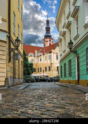 Stretta strada acciottolata tra edifici colorati come una chiesa cattolica sullo sfondo nella città vecchia di Praga, Repubblica Ceca. Foto Stock