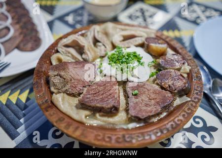 Piatto tradizionale asiatico kazako Beshbarmak: Tagliatelle con agnello e cipolle da vicino su un piatto sul tavolo. vicino al brodo in ciotole. dastarkhan. bolied Foto Stock