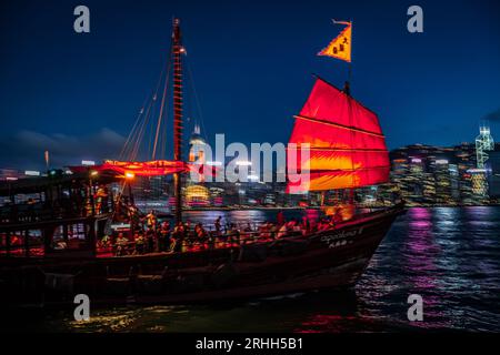 Splendida vista notturna di una junk boat luminosa nel Victoria Harbour di fronte al fantastico skyline di Hong Kong con i suoi impressionanti grattacieli Foto Stock