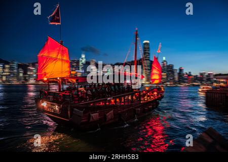 Splendida vista notturna di una junk boat luminosa nel Victoria Harbour di fronte al fantastico skyline di Hong Kong con i suoi impressionanti grattacieli Foto Stock