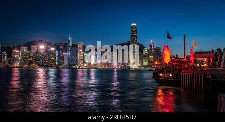 Splendida vista notturna di una junk boat luminosa nel Victoria Harbour di fronte al fantastico skyline di Hong Kong con i suoi impressionanti grattacieli Foto Stock