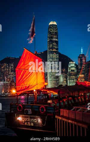 Splendida vista notturna di una junk boat luminosa nel Victoria Harbour di fronte al fantastico skyline di Hong Kong con i suoi impressionanti grattacieli Foto Stock