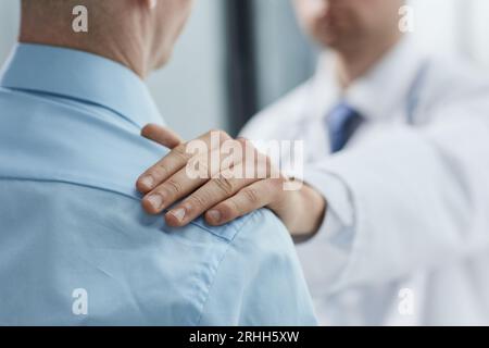 Un medico di sesso maschile parla con un paziente di sesso maschile che la sostiene e la conforta durante la reception. Foto Stock