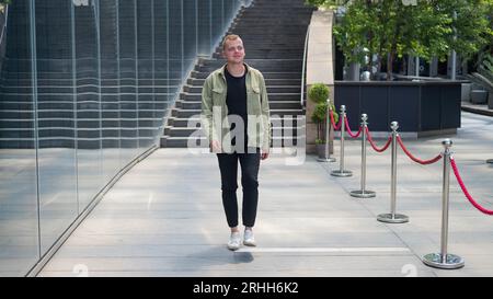 Joyful caucasian Guy passa davanti a un edificio commerciale. Foto Stock