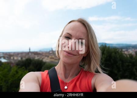 Una giovane e bella donna in un abito arancione brillante si erge sullo sfondo del panorama di Firenze e gode della vista della città di Bobol Foto Stock