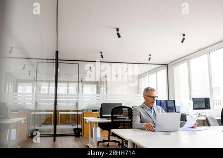 Un uomo d'affari maturo e serio che si occupa del lavoro di carta, un manager dai capelli grigi che lavora con conti e documenti, un uomo che lavora in un ufficio moderno, un investitore di successo che esamina i report finanziari Foto Stock