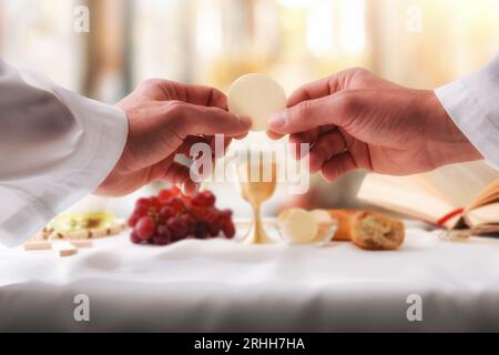 Mani di un sacerdote che consacra un ospite come corpo di Cristo per distribuirlo ai comunicanti sull'altare Foto Stock