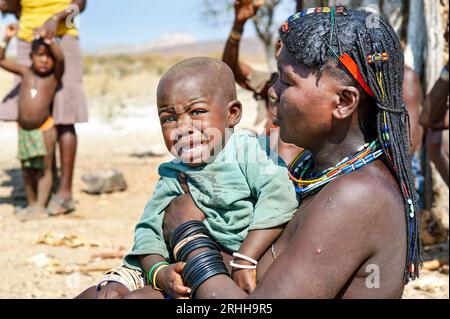 Namibia. Ritratto di una giovane donna del gruppo etnico Zemba Bantu con il suo bambino in lacrime, nella regione di Kunene Foto Stock