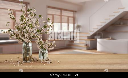 Tavolo in legno, scrivania o mensola da vicino con rami di fiori di ciliegio in vaso di vetro con vista sfocata dei japandi bagno con scala, minimalista Foto Stock