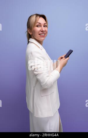 giovane donna blondie caucasica piuttosto sottile in giacca bianca e vestito su uno sfondo semplice Foto Stock
