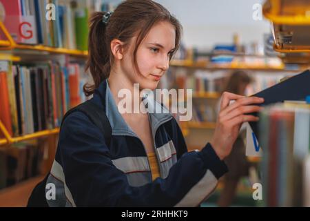 Studentessa che cerca e sceglie i libri da una libreria della biblioteca. Istruzione, letteratura e concetti di nuova edizione. Foto Stock